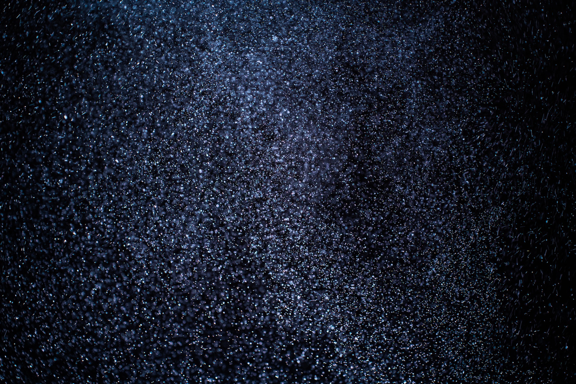 Organic dust particles floating on a colorful light beam on black background.