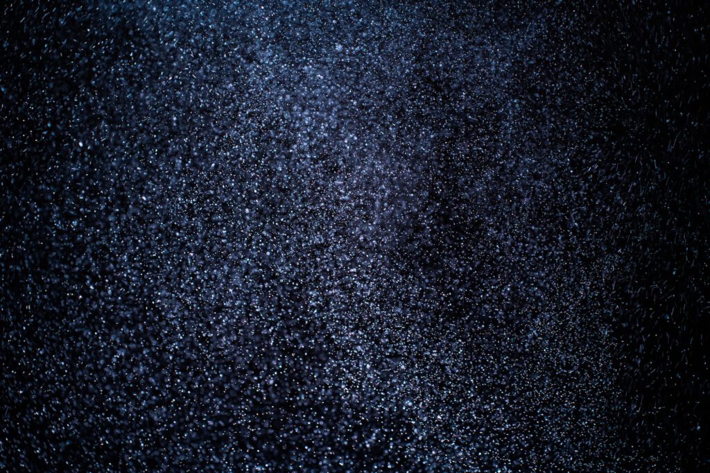 Organic dust particles floating on a colorful light beam on black background.