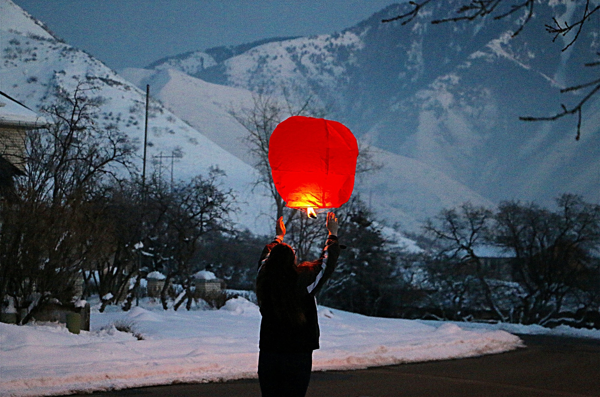 Woman from behind preparing to release a red lantern skyward in celebration of Chinese New Year.